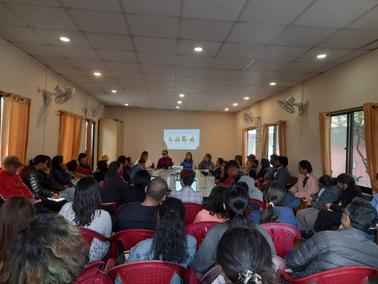 Group photo of the event where the panelists are sitting at the very front and the group of people are watching them 