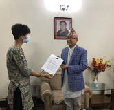 Photo of Shubha handing the letter to Dinesh Thapalaiya, Chief of the Election Comission of Nepal